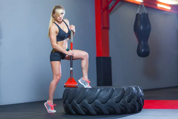 Fitness vrouw raken wiel band met hamer slee in de sportschool. — Stockfoto