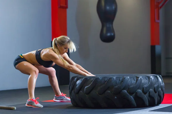 Apto atleta feminino exercitando-se com um pneu enorme, puxa no ginásio. Crossfit mulher exercitando com pneu grande — Fotografia de Stock