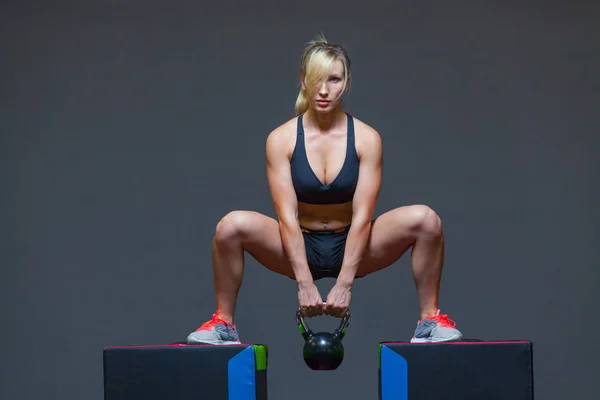 Жінка займається в спортзалі з вагою чайника, на кубиках — стокове фото