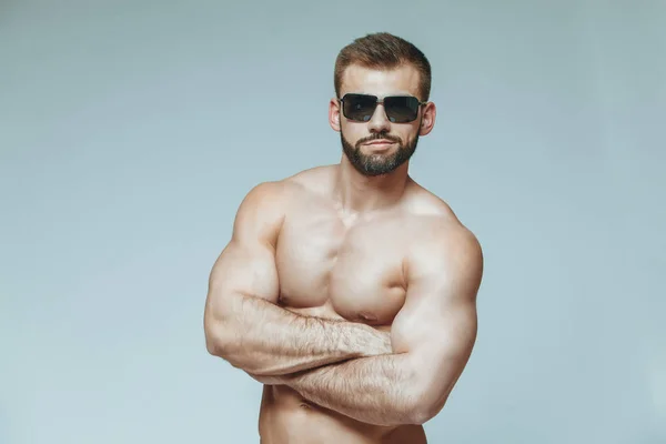.bodybuilder posing. Beautiful sporty guy male power. Fitness muscled in blue shorts and sunglasses. on isolated grey background. Man with muscular torso. Strong Athletic Man Fitness Model Torso — Stock Photo, Image
