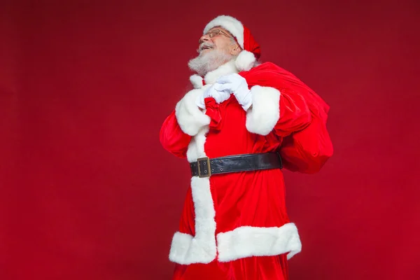 Weihnachten. Der freundliche und müde Weihnachtsmann in weißen Handschuhen trägt eine rote Tasche mit Geschenken über der Schulter. isoliert auf rotem Hintergrund. — Stockfoto