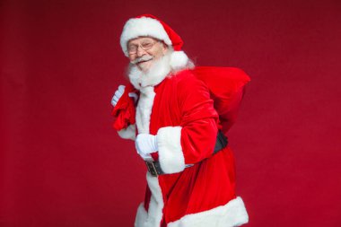 Noel. Tür ve beyaz eldiven yorgun Noel Baba'ya omzunun üzerinden hediyeler ile kırmızı bir çanta taşıyor. Kırmızı zemin üzerine izole.