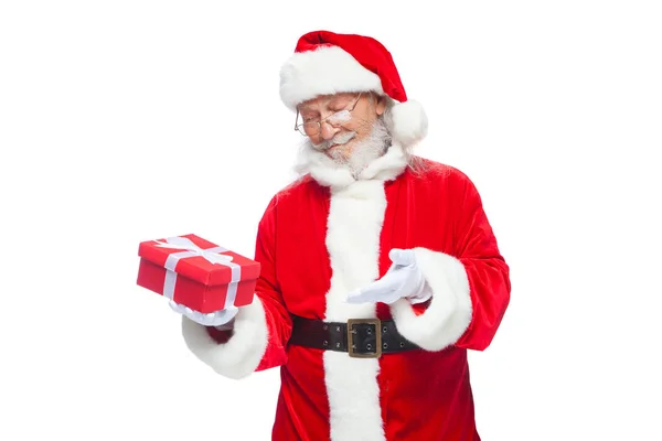 Navidad. Santa Claus sonriente con guantes blancos sostiene una caja roja de regalo con un lazo. Señalando el regalo. Aislado sobre fondo blanco . — Foto de Stock