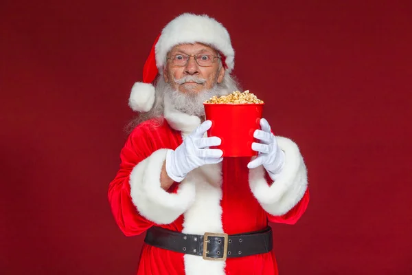 Natale. Babbo Natale in guanti bianchi che tiene un secchio rosso di popcorn con due mani, lo sposta in avanti e si offre di trattare. Il concetto di visitare un cinema, guardare un film con i popcorn. Isolato — Foto Stock