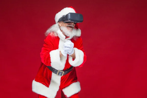 Noël. Père Noël en noir lunettes de réalité virtuelle fait des gestes avec ses mains. Surprise, émotion. Nouvelle technologie. Isolé sur fond rouge . — Photo