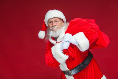 Noel. Tür ve beyaz eldiven yorgun Noel Baba'ya omzunun üzerinden hediyeler ile kırmızı bir çanta taşıyor. Kırmızı zemin üzerine izole.