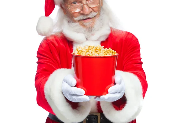 Natale. Babbo Natale in guanti bianchi che tiene un secchio rosso di popcorn con due mani, lo sposta in avanti e si offre di trattare. Il concetto di visitare un cinema, guardare un film con i popcorn. Isolato — Foto Stock