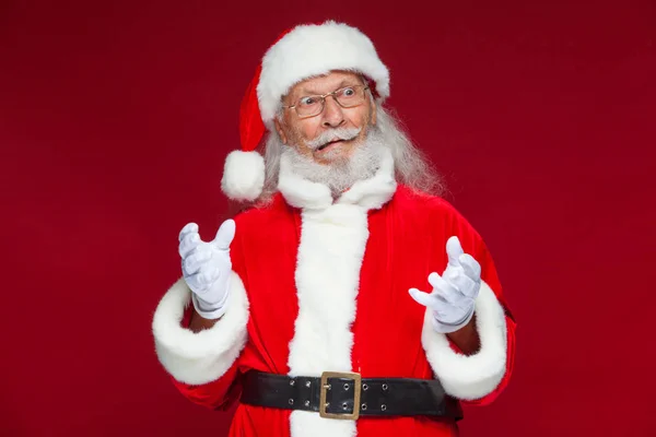 Weihnachten. Der gute Weihnachtsmann in weißen Handschuhen zeigt Gesichter, Fratzen, zeigt seine Zunge. nicht das Standardverhalten. isoliert auf rotem Hintergrund. — Stockfoto