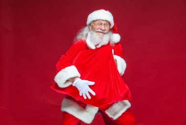 Noel. Bir gülümseyen Noel Baba ile kırmızı bir torba tutarak onun önünde onu kucaklayan sunar. Kırmızı zemin üzerine izole.