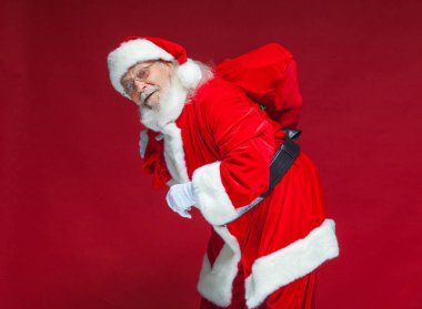 Noel. Tür ve beyaz eldiven yorgun Noel Baba'ya omzunun üzerinden hediyeler ile kırmızı bir çanta taşıyor. Kırmızı zemin üzerine izole.