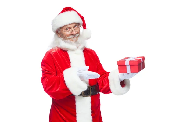 Christmas. Smiling Santa Claus in white gloves is holding a gift red box with a bow. Pointing at the gift. Isolated on white background. — Stock Photo, Image