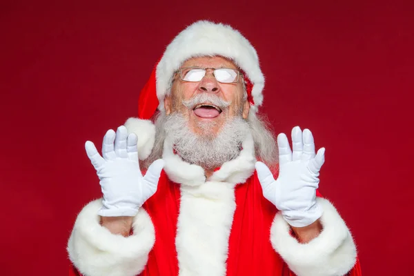 Weihnachten. Der gute Weihnachtsmann in weißen Handschuhen zeigt Gesichter, Fratzen, zeigt seine Zunge. nicht das Standardverhalten. isoliert auf rotem Hintergrund. — Stockfoto