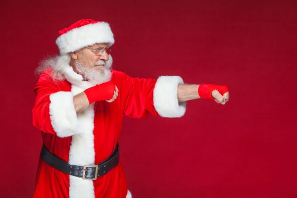 Weihnachten. Weihnachtsmann mit roten Bandagen, die sich um seine Hände wickeln, um Tritte zu imitieren. Kickboxen, Karate, Boxen. isoliert auf rotem Hintergrund. — Stockfoto