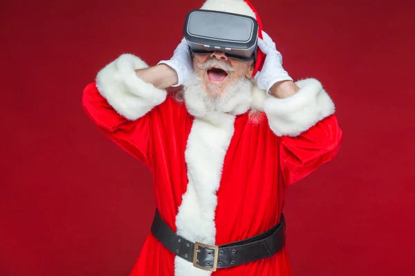 Natale. Babbo Natale in nero occhiali realtà virtuale fa gesti con le mani. Sorpresa, emozione. Nuove tecnologie. Isolato su sfondo rosso . — Foto Stock