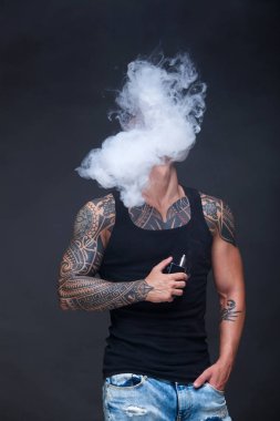 Vaper. Dövmeli kas bir gövde adamla koyu arka plan üzerinde elektronik sigara duman