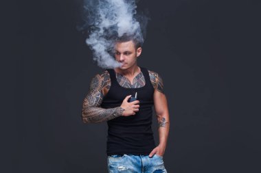 Vaper. Dövmeli kas bir gövde adamla koyu arka plan üzerinde elektronik sigara duman