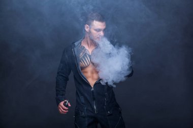 Vaper. Dövmeli bir kaslı çıplak gövde adamla koyu arka plan üzerinde elektronik sigara duman