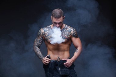 Vaper. Dövmeli bir kaslı çıplak gövde adamla koyu arka plan üzerinde elektronik sigara duman