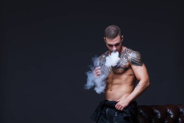 Vaper. Dövmeli bir kaslı çıplak gövde adamla koyu arka plan üzerinde elektronik sigara duman