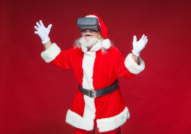 Noel. Noel Baba siyah sanal gerçeklik bardaklarda elleriyle hareketleri yapar. Sürpriz, duygu. Yeni teknoloji. Kırmızı zemin üzerine izole.