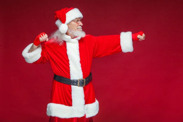 No Natal. Papai Noel com ligaduras vermelhas ferida em suas mãos para boxe imita chutes. Kickboxing, karaté, boxe. Isolado em fundo vermelho . — Fotografia de Stock