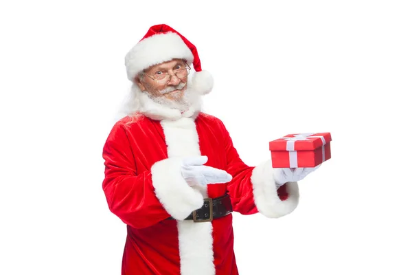 Navidad. Santa Claus sonriente con guantes blancos sostiene una caja roja de regalo con un lazo. Señalando el regalo. Aislado sobre fondo blanco . — Foto de Stock