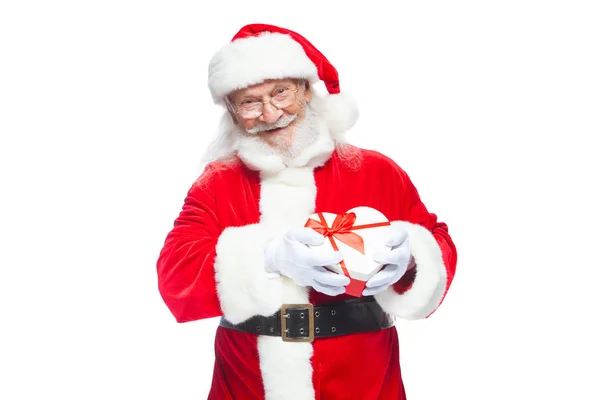 Navidad. Santa Claus sonriente con guantes blancos sostiene una caja de regalo en forma de corazón rojo y blanco con una cinta roja. Aislado sobre fondo blanco . — Foto de Stock