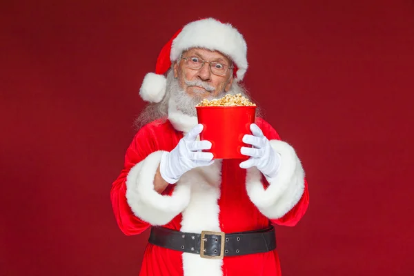 Natale. Babbo Natale in guanti bianchi che tiene un secchio rosso di popcorn con due mani, lo sposta in avanti e si offre di trattare. Il concetto di visitare un cinema, guardare un film con i popcorn. Isolato — Foto Stock
