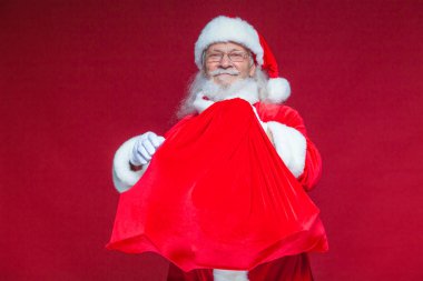 Noel. Bir gülümseyen Noel Baba ile kırmızı bir torba tutarak onun önünde onu kucaklayan sunar. Kırmızı zemin üzerine izole.