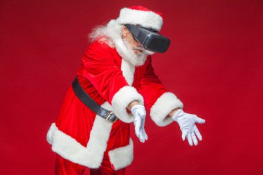 Noel. Noel Baba siyah sanal gerçeklik bardaklarda elleriyle hareketleri yapar. Sürpriz, duygu. Yeni teknoloji. Kırmızı zemin üzerine izole.