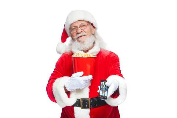 Natale. Sorridente, buon Babbo Natale in guanti bianchi in possesso di un secchio rosso di popcorn in una mano, e un telecomando TV con la sua seconda mano e cambia canale. Il concetto di guardare un film — Foto Stock