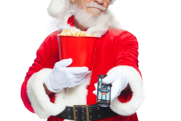 Natale. Sorridente, buon Babbo Natale in guanti bianchi in possesso di un secchio rosso di popcorn in una mano, e un telecomando TV con la sua seconda mano e cambia canale. Il concetto di guardare un film — Foto Stock
