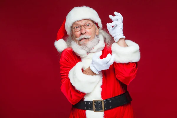 Weihnachten. Der gute Weihnachtsmann in weißen Handschuhen zeigt Gesichter, Fratzen, zeigt seine Zunge. nicht das Standardverhalten. isoliert auf rotem Hintergrund. — Stockfoto