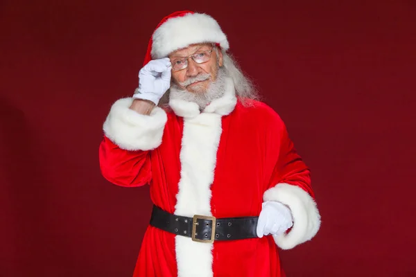 Рождество. Серьезный Санта-Клаус в белых перчатках настраивает очки и смотрит в камеру. Изолированный на красном фоне . — стоковое фото