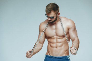 .vücut geliştirmeci poz. Güzel sportif adam erkek güç. Fitness mavi şort ve güneş gözlüğü kaslı. izole gri arka plan üzerinde. Kas gövde olan adam. Güçlü atletik erkek Fitness modeli gövde