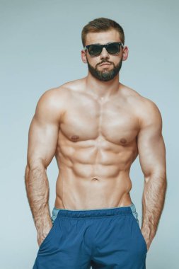 .vücut geliştirmeci poz. Güzel sportif adam erkek güç. Fitness mavi şort ve güneş gözlüğü kaslı. izole gri arka plan üzerinde. Kas gövde olan adam. Güçlü atletik erkek Fitness modeli gövde
