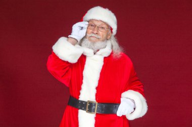 Noel. Beyaz eldiven ciddi Noel Baba'ya onun gözlük ayarlar ve kameraya bakıyor. Kırmızı zemin üzerine izole.