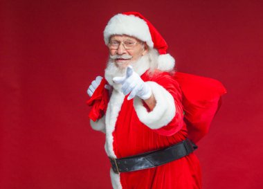 Noel. Noel Baba hediye onun arkasında bir torba ile beyaz eldiven gülümseyen onun parmağı kameraya çekiyor. Kırmızı zemin üzerine izole.