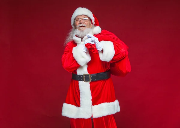 Weihnachten. Der freundliche und müde Weihnachtsmann in weißen Handschuhen trägt eine rote Tasche mit Geschenken über der Schulter. isoliert auf rotem Hintergrund. — Stockfoto