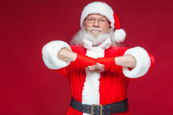 Jul. Jultomte med röda bandage sår på händerna för boxning imiterar sparkar. Kickboxning, karate, boxning. Isolerad på röd bakgrund. — Stockfoto