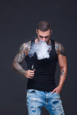 Vaper. Dövmeli kas bir gövde adamla koyu arka plan üzerinde elektronik sigara duman