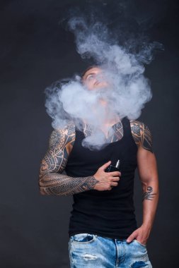 Vaper. Dövmeli kas bir gövde adamla koyu arka plan üzerinde elektronik sigara duman