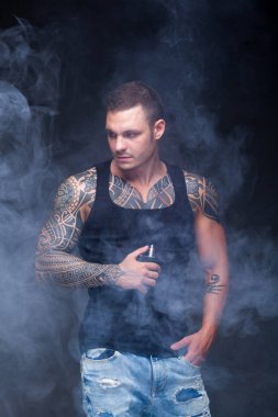 Vaper. Dövmeli kas bir gövde adamla koyu arka plan üzerinde elektronik sigara duman