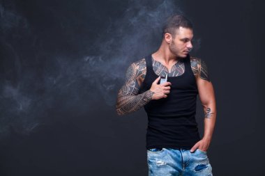 Vaper. Dövmeli kas bir gövde adamla koyu arka plan üzerinde elektronik sigara duman