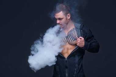Vaper. Dövmeli bir kaslı çıplak gövde adamla koyu arka plan üzerinde elektronik sigara duman
