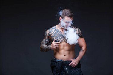 Vaper. Dövmeli bir kaslı çıplak gövde adamla koyu arka plan üzerinde elektronik sigara duman