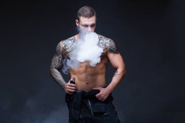 Vaper. Dövmeli bir kaslı çıplak gövde adamla koyu arka plan üzerinde elektronik sigara duman