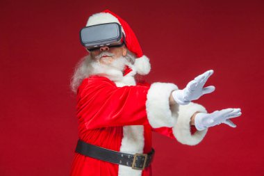 Noel. Noel Baba siyah sanal gerçeklik bardaklarda elleriyle hareketleri yapar. Sürpriz, duygu. Yeni teknoloji. Kırmızı zemin üzerine izole.
