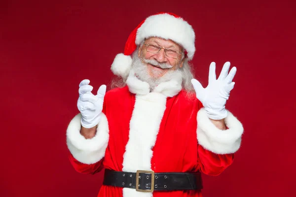 Weihnachten. Der gute Weihnachtsmann in weißen Handschuhen zeigt Gesichter, Fratzen, zeigt seine Zunge. nicht das Standardverhalten. isoliert auf rotem Hintergrund. — Stockfoto