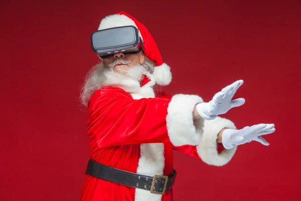 Natale. Babbo Natale in nero occhiali realtà virtuale fa gesti con le mani. Sorpresa, emozione. Nuove tecnologie. Isolato su sfondo rosso . — Foto Stock